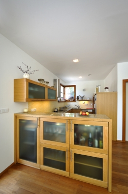 Kuchyň se ukrývá „za rohem“, aby z obývacího pokoje nebylo vidět na pracovní plochu. Linka s dvířky z dubového dřeva je prostorově ohraničena barovým pultem s vestavěnými skříňkami a nikou pro servírovací vozík.
