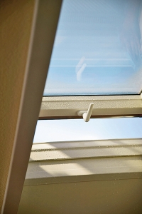 Výklopné plastové střešní okno s kličkou z tvrzeného plastu nastavené do polohy „otevřeno“ (Roto).