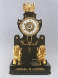 Portálové empírové hodiny, první čtvrtina 19. století, na černém obdélníkovém soklu z černého leštěného dřeva dva titáni nesoucí portál, apliky tlačená mosaz, výška 65 cm.