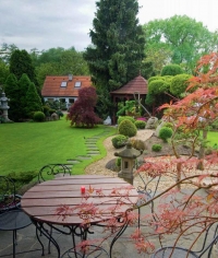 Pohled z terasy na střední část zahrady s čajovým domkem a dominantní Picea omorikou.
