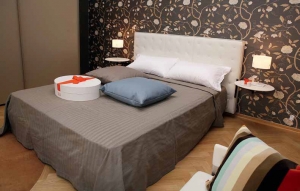 Tapeta se stylizovaným květinovým dekorem vytváří v ložnici intimní ovzduší. Postel Jack s masivním koženým čelem, nočními stolky a ergonomickou matrací nabízí pohodlné spaní.