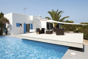 Sněhobílé omítky, blankytné nebe a modré okenice jsou pro španělské Středomoří typické. Vyvýšená betonová deska nad bazénem tvoří terasu a zároveň zastřešuje technické zázemí domu, které se pod ní ukrývá, zapuštěné ve svahu.