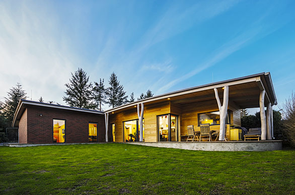 Dřevostavba může být omítnuta, obložena dřevem i jiným materiálem. Bungalov pasivní dřevostavby z masivních komponentů DEK panel navrhla Ing. Irena Truhlářová. Sloupky ve tvaru kmenů stromů podpírají přesahující střechu a evokují bydlení v lese.