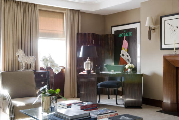 Materiály tohoto exkluzivního interiéru ve stylu art deco jsou opravdu luxusní: profilovaná kovová područka křesílka si skvěle rozumí s lesklým květníkem orchideje, dřevěný obklad krbu působí jako nábytkový solitér a bohatě řasené závěsy vytvářejí sošce koně téměř až divadelní pozadí. Uklidňující kombinaci barev bílé kávy a hořké čokolády příjemně narušují tmavý stůl a paraván. Hrozící nudu interiéru barevně koncipovaného tzv. „tón v tónu“ odvracejí nepřehlédnutelná umělecká díla.
